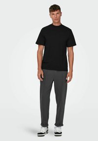 Zwarte korte mouwen t-shirt gecombineerd met grijze taps toelopende broek, met een gladde textuur en een eenvoudig, minimalistisch ontwerp.