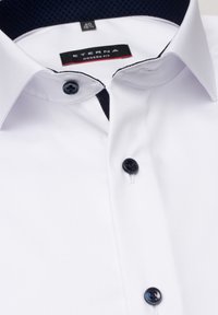 Camicia bianca con bottoni, dal taglio moderno, con colletto in contrasto di un blu navy scuro e bottoni neri, realizzata in tessuto morbido.