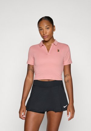 Roze cropped polo met een kraag en logo, gecombineerd met een zwarte sportieve skort met een gladde textuur en subtiele Nike-branding.