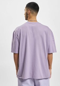 Jasnofioletowy bawełniany t-shirt o luźnym kroju, z krótkimi rękawami i okrągłym dekoltem. Gładka faktura i minimalne detale.