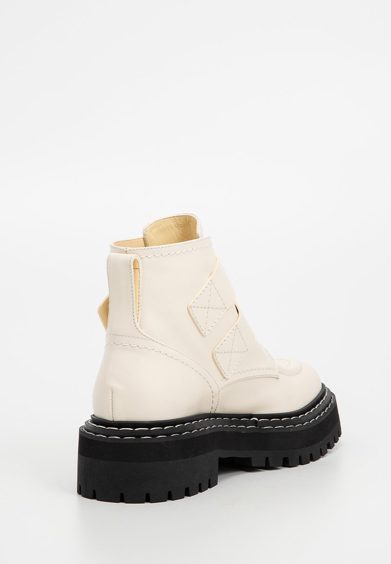 Grube botki za kostkę, z kremowej, gładkiej skóry z akcentami w formie wycięć oraz czarną, grubą gumową podeszwą z bieżnikiem.