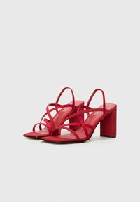 Rote High-Heelsandalen mit mehreren Kreuzriemen. Quadratische Zehen und einen klobigen Blockabsatz. Glatte Textur mit glänzender Oberfläche.