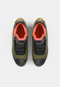 Sneakers w kolorze oliwkowym i czarnym, z teksturowaną powierzchnią, jasnoróżowym podszyciem i odblaskowymi akcentami. Posiadają sznurowadła i wyściełaną podeszwę.