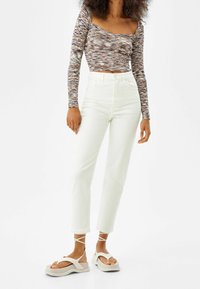 Långärmad, åtsittande topp i flerfärgad mönster; högmidjade, raka vita jeans; kraftiga, ljusa sandaler med anklar.