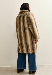 Faux-Fellmantel in Brauntönen mit Kragen, langen Ärmeln und einem leicht übergroßen Schnitt, kombiniert mit weit geschnittenen blauen Jeans.