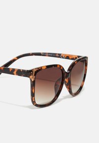Tortoiseshell sunglasses with a bold cat-eye shape, featuring gradient brown lenses and black-orange patterned frames.