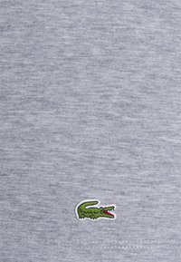 Tricou din bumbac gri cu un finisaj texturat, având un mic logo brodat cu un crocodil verde în colțul stâng jos.