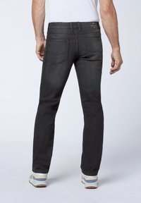Black denim jeans with a slim fit, two back pockets, and a slight stretch. Worn with light-colored sneakers, showing ankle cuffs.