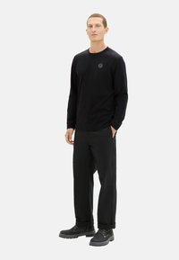 Zwarte lange mouwen shirt met een ronde hals en een klein logo, gecombineerd met zwarte loszittende broek en zwarte veterschoenen.