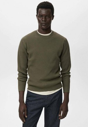 Suéter de punto en verde oliva con mangas largas, cuello redondo, superpuesto sobre una camisa de color claro. Textura suave, ajuste casual.