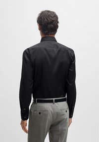 Black long-sleeve shirt with a smooth finish, featuring a classic collar and buttoned cuffs, paired with light gray trousers.