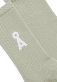 Chaussettes vertes à côtes en tissu doux, ornées d'un logo blanc en forme de lettre "a". La texture est lisse, avec une coupe ajustée.