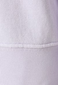 Tissu en maille violet à finition texturée, avec un ourlet côtelé lisse et des détails de couture visibles le long des bords.