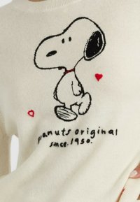 Maglione bianco con un design lavorato a maglia di Snoopy in nero e rosso, caratterizzato da accenti a forma di cuore rossi e dal testo "peanuts original dal 1950."