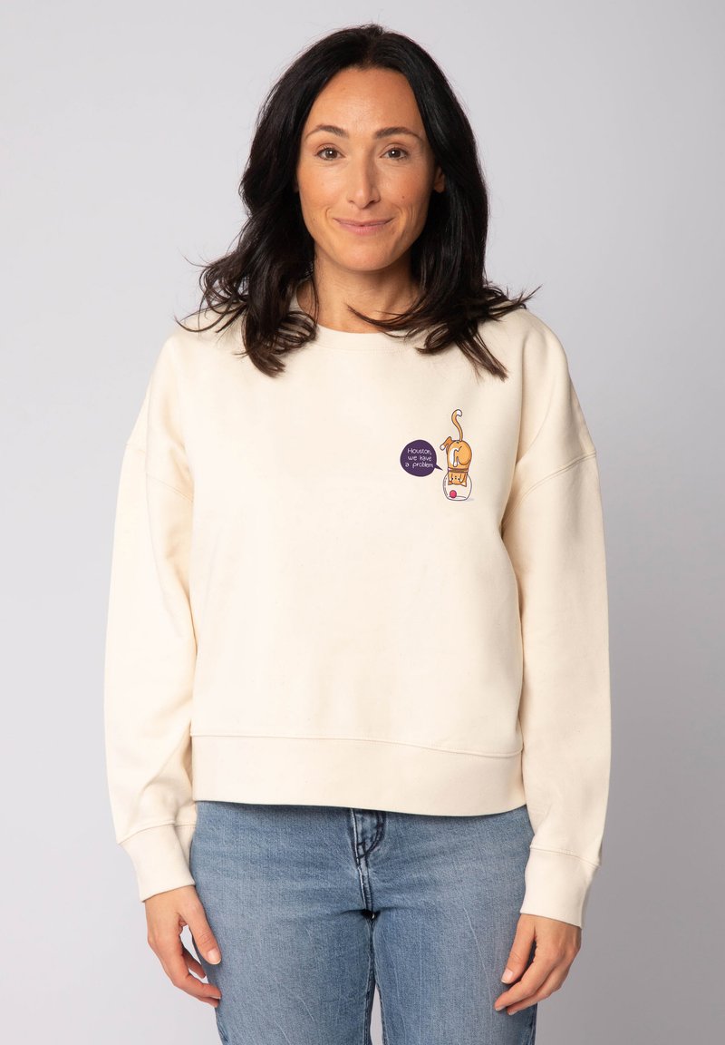 Sweatshirt couleur crème à coupe décontractée, avec un petit graphique d'un chat et du texte sur le devant. Matière en mélange de coton doux.