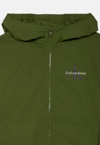 Olivovozelená kapucňová bunda s plným zipsom, elastickými manžetami a diskrétnym logom Calvin Klein v bielej a tmavosivej farbe na prednej strane.