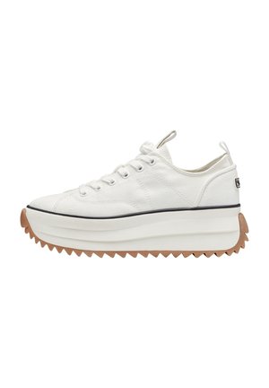 Vit canvastennis med en texturerad yta, med en tjock, räfflad gummisula i beige och svarta accenter, samt en dragflik på hälen.
