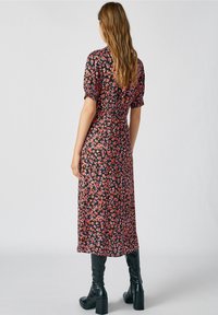 Vestido maxi floral con mangas cortas abullonadas, con una base negra, un patrón de flores rojas y rosas, y una cintura ajustada. Llevado con botas altas negras hasta la rodilla.