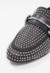 Mocassin en cuir noir orné de clous métalliques argentés sur toute la surface et d'une bride décorative argentée sur le dessus.