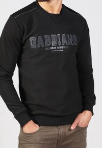 Sudadera negra de manga larga, con cuello redondo, texto impreso en gris, con puños y dobladillo de canalé. Textura suave, corte casual.
