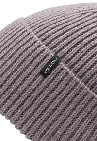 Grå strikket hue med vertikal ribbing, med et sort mærke der viser "VOLCOM" syet på siden. Blødt stof og tætsiddende design.