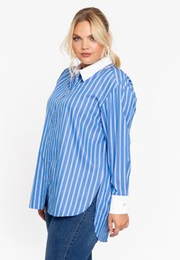 Blauw-wit gestreepte button-up shirt met een witte kraag, lange mouwen en een afgeronde zoom. De stof lijkt glad met een lichte glans.
