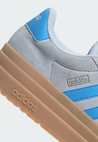 Grå mockaskor med blå detaljer och tre sidosträck. Utrustad med en chunkig beigefärgad gummisula och metallisk logotypdetalj.