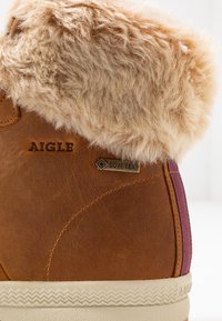 Bruine leren laars met een pluizige beige nepbontkraag, GORE-TEX-logo en paarse accenten. Textuur rubberen zool met zigzagpatroon.