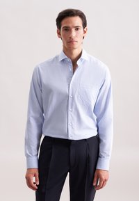 Camicia a maniche lunghe blu chiaro realizzata in tessuto intrecciato, con chiusura frontale a bottoni, colletto a punta e tasca applicata sul lato sinistro del petto.