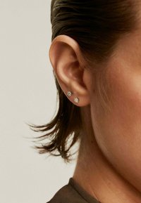 Pendientes de plata en forma de estrella con piedras transparentes redondas y facetadas, engastadas en un metal texturizado, llevados en un primer plano de la oreja de un modelo.