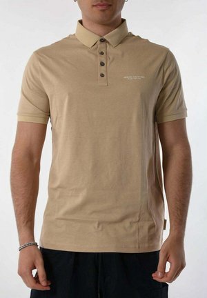 Polo en coton beige avec un col, trois boutons foncés et un petit logo sur la poitrine gauche. Manches courtes et coupe décontractée.