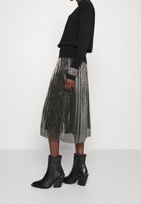 Suéter negro con dobladillo acanalado, combinado con una falda midi plisada plateada y botas de tacón negro hasta el tobillo. La falda presenta una textura brillante.