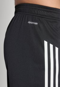 Un short de sport noir avec une taille élastique, un logo "AEROREADY" blanc et trois bandes blanches sur le côté. Texture lisse.