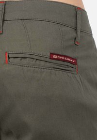 Pantalons khaki avec une surface texturée, dotés de coutures rouges et d'une étiquette rouge avec "CIPO & BAXX" sur la poche arrière.