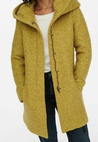 Gelber Wollmantel mit strukturierter Oberfläche, Kapuze und Knopfverschluss. Verfügt über zwei seitliche Taschen und eine lockere Passform. Wird über einem leichten Pullover getragen.