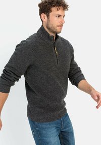 Dunkelgrauer Half-Zip-Pullover mit geripptem Kragen und Bündchen, texturiertem Stoff und einem kleinen Reißverschlussdetail. Kombiniert mit blauen Jeans.