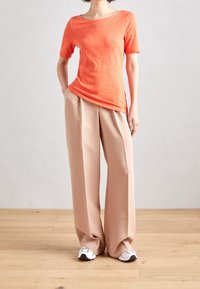 Top arancione a maniche corte con scollo a barco, abbinato a pantaloni beige larghi e sneakers bianche. Tessuto liscio e vestibilità comoda.