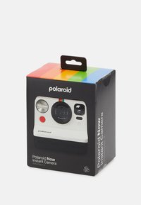 L'emballage de l'appareil photo instantané Polaroid Now présente une illustration blanche de l'appareil, une boîte noire avec un dessus rayé coloré et des détails de marque clés.