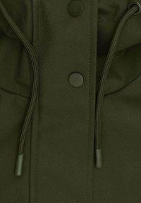 Oliwkowa kurtka z fakturowanej tkaniny, z dwoma czarnymi guzikami, regulowanymi sznurkami i gładkim zamkiem błyskawicznym.