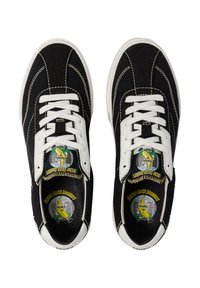 Baskets en toile noires avec des lacets blancs, semelles en caoutchouc et surpiqûres blanches contrastantes. Présente un logo de banane coloré sur la semelle intérieure.