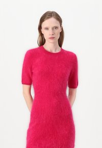 Fuchsia Strickkleid mit kurzen Ärmeln, das eine weiche, flauschige Textur und ein vertikales Rippenmuster aufweist. Figurbetonte Silhouette.