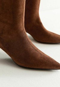 Stivaletti alla caviglia in suede marrone con punta affusolata e silhouette elegante. Presentano una texture liscia e dettagli di cucitura discreti.