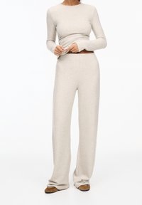 Haut à manches longues en maille beige et pantalon à jambes larges, avec une texture douce et une coupe ajustée. Tenue décontractée avec une silhouette relaxante.