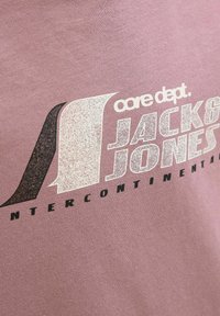 Lila Baumwoll-T-Shirt mit kurzen Ärmeln, das ein grafisches Druckmotiv mit "core dept." und "JACK & JONES INTERCONTINENTAL" in weißem und schwarzem Text zeigt.