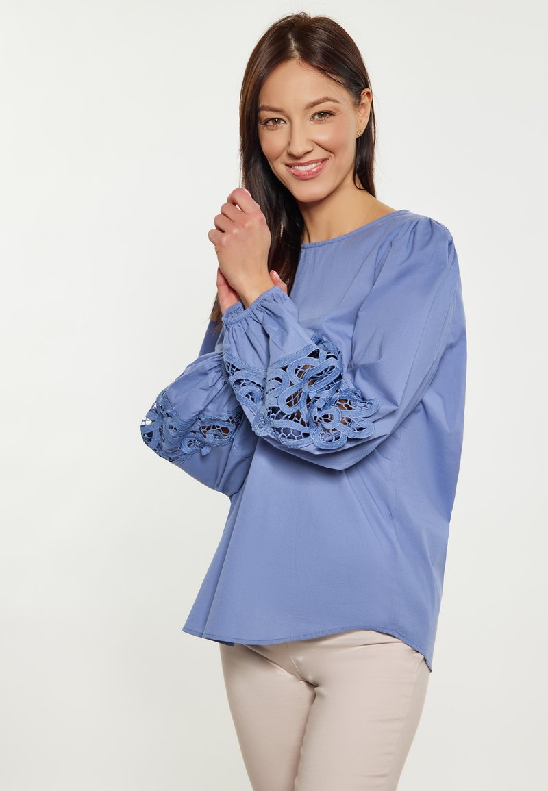 Blusa azzurro chiaro con maniche voluminose caratterizzata da dettagli in pizzo intricati. Tessuto morbido, scollatura rotonda e vestibilità comoda.