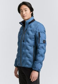 Luftige Steppjacke in Hellblau mit strukturiertem Quilt, hohem Kragen, durchgehendem Reißverschluss und seitlichen Taschen. Verfügt über eine kleine Armtasche mit Logo.