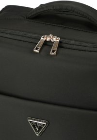 Schwarze synthetische Tasche mit glatter Textur, ausgestattet mit einem oberen Reißverschluss mit metallischen Beschlägen und einem dreieckigen Logobadge auf der Vorderseite.