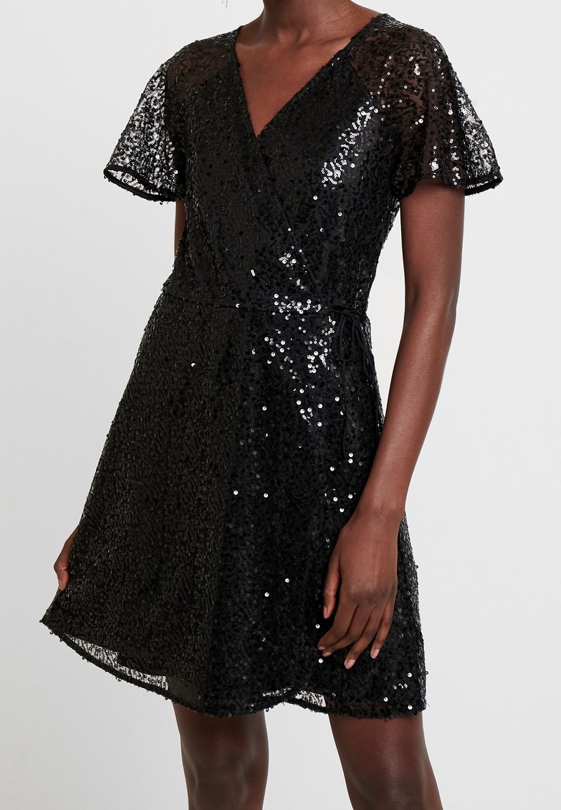 Robe noire pailletée avec un décolleté en V, des manches courtes à volants et une taille nouée. Le tissu présente une texture brillante avec des détails en sequins élaborés.