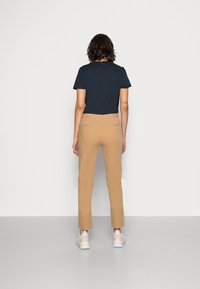 Granatowa koszulka z krótkim rękawem w zestawieniu z beżowymi spodniami slim-fit i białymi trampkami. Materiał wydaje się gładki, z dopasowanym krojem.