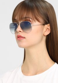 Aviator sunglasses with a silver metal frame, gradient blue lenses, and thin wire temples, featuring a subtle logo near the lenses.